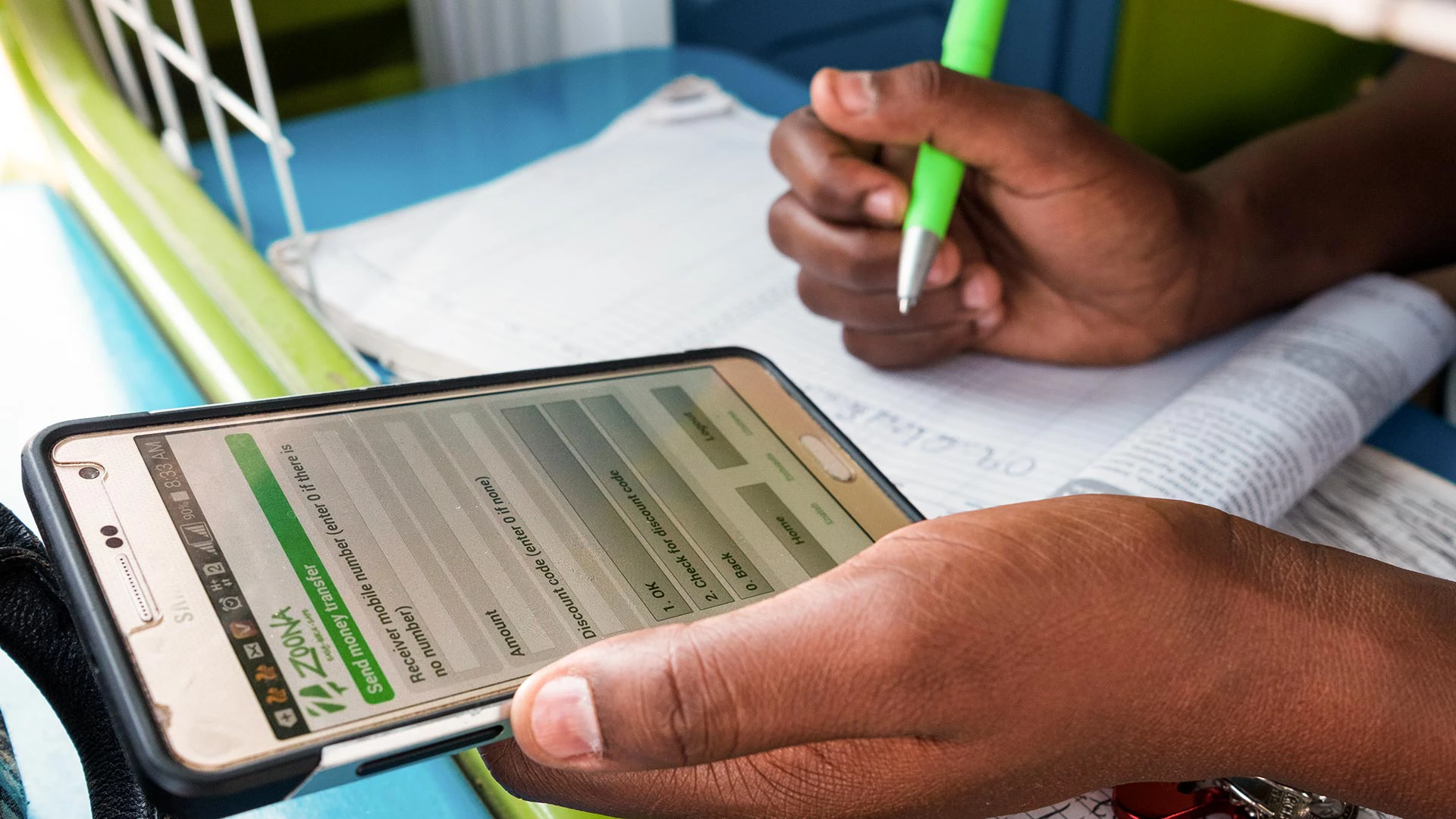 A money transfer user interface on a smartphone in the hand Susan Mwango, a Zoona teller, in the booth she operates in Lusaka, Zambia on 9 January 2018. Zoona is an innovative money transfer platform that is one of a new breed of digital financial services on the African continent. Photo © Nyani Quarmyne/International Finance Corporation